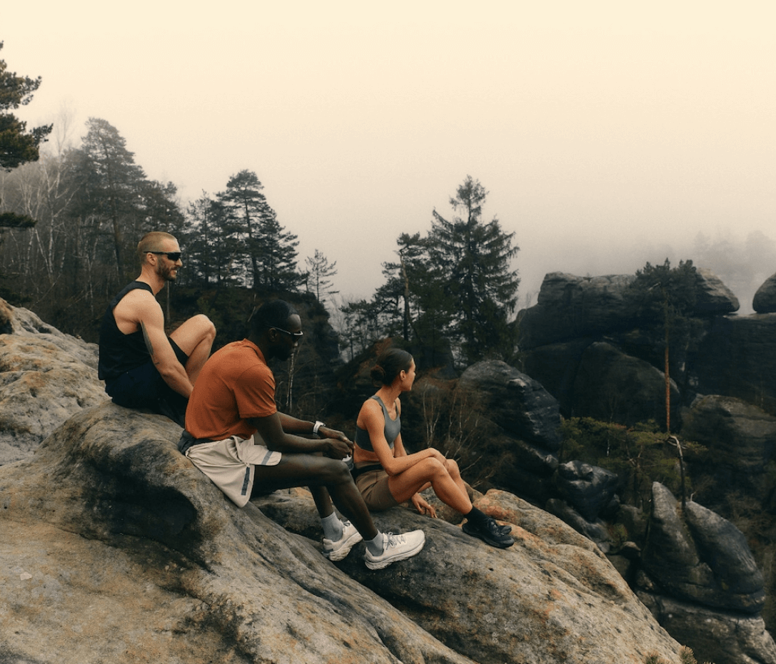 A group of young people are sitting on large stones in nature.