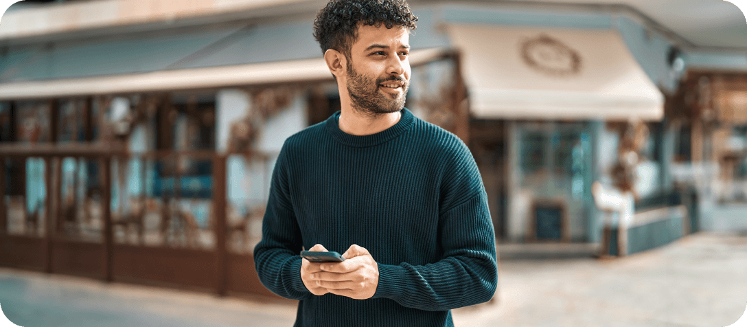 Young guy in dark green jumper smiling and holding phone in hands.